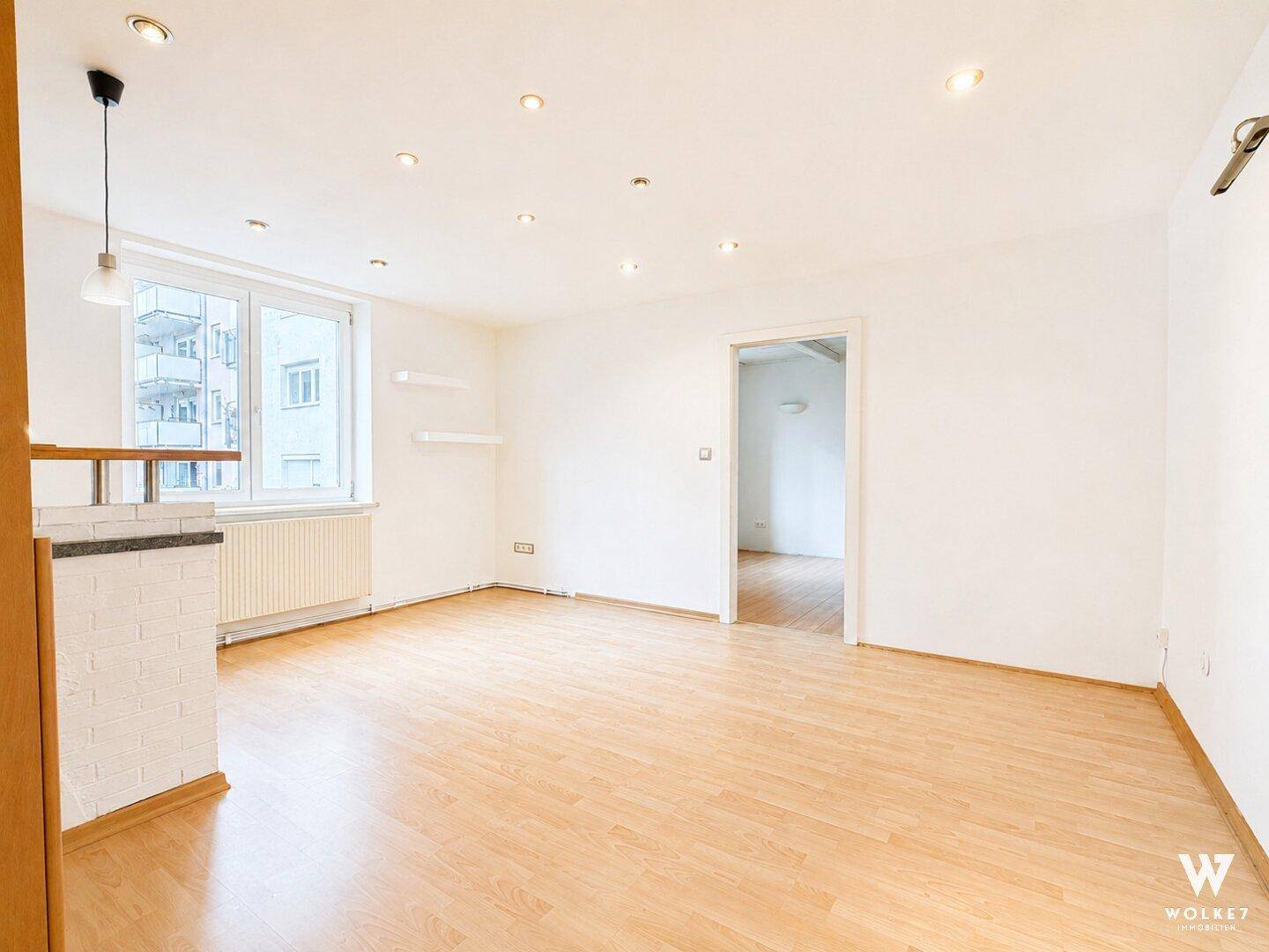 Geräumiges Wohnzimmer mit hellem Holzboden und Blick auf die umliegenden Gebäude.