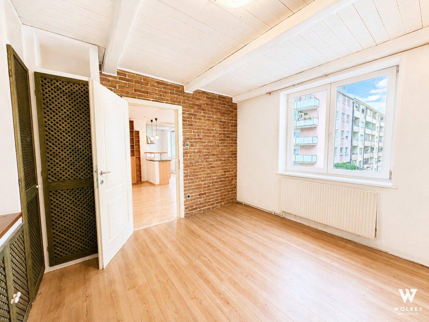 Zimmer mit Holzbalkendecke, Holzboden und einer Akzentwand aus Ziegeln.