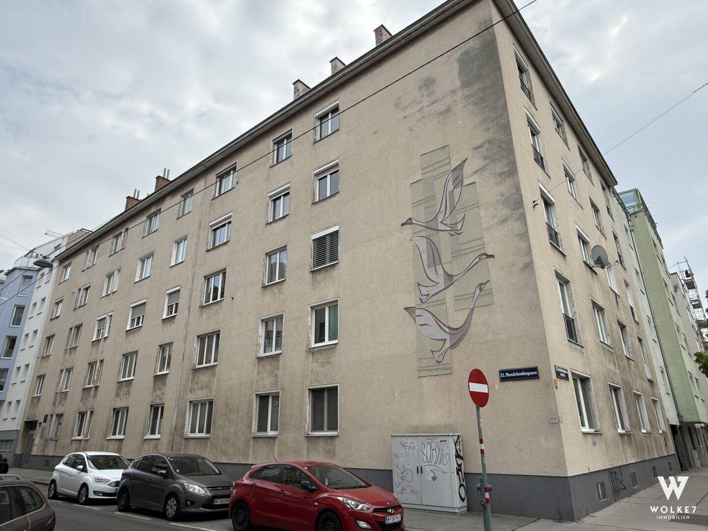 Eckgebäude mit einer Wandmalerei und parkenden Autos an der Straße.