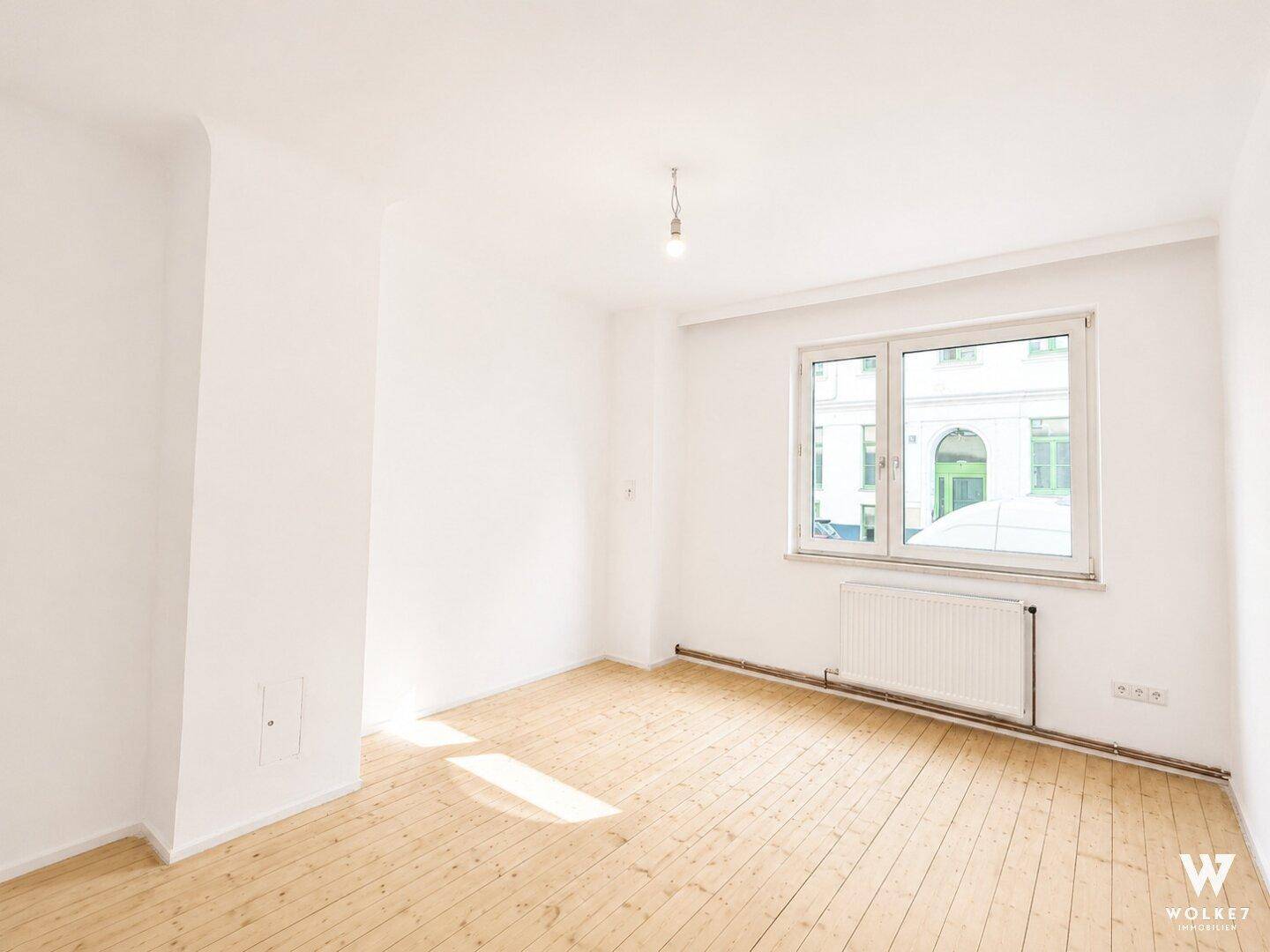Heller, leerer Raum mit Dielenboden und großem Fenster, bietet viel natürliches Licht.