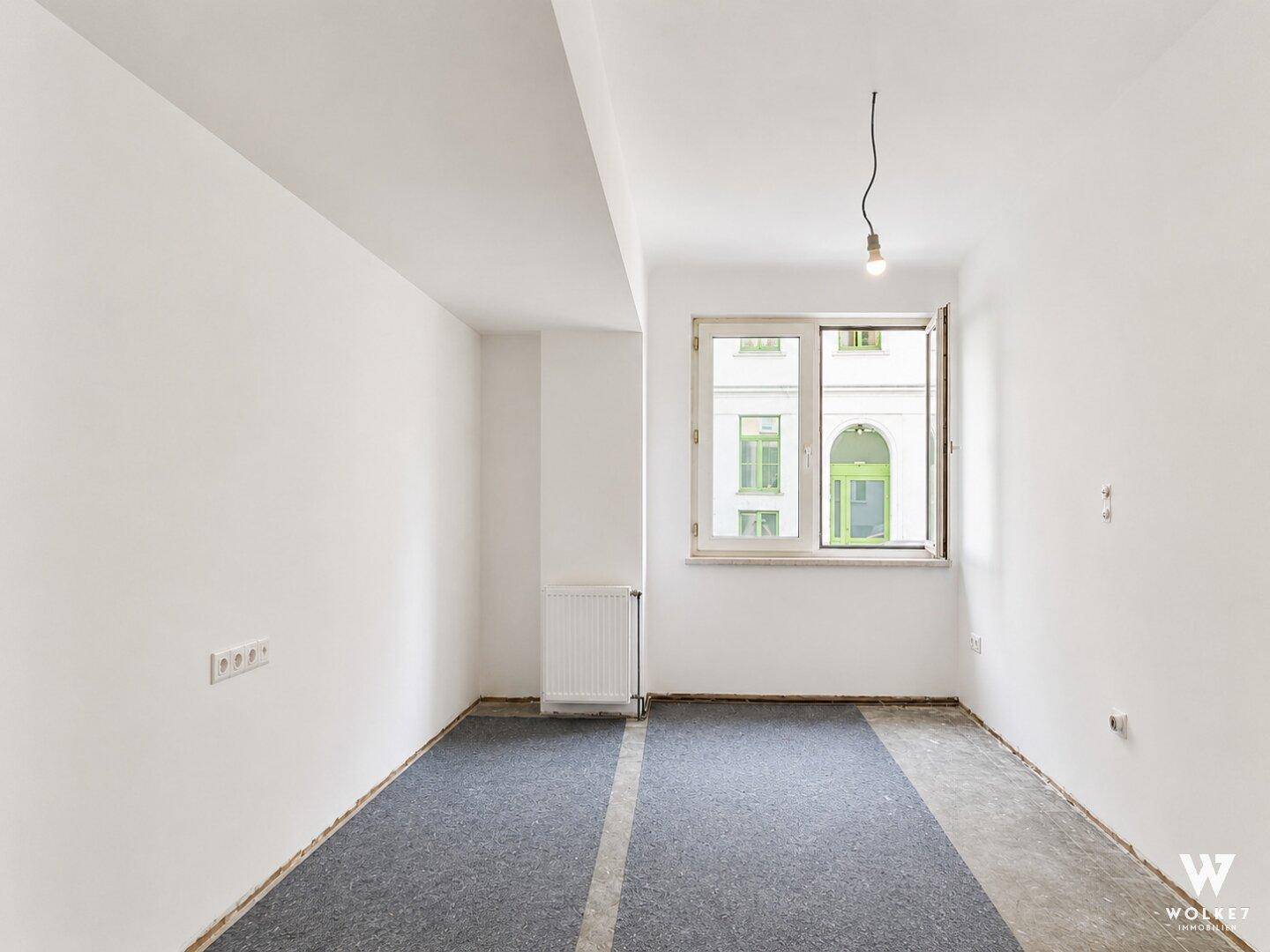 Leerer Raum mit Fenster und teilweise verlegtem Teppichboden, bereit für die Fertigstellung.
