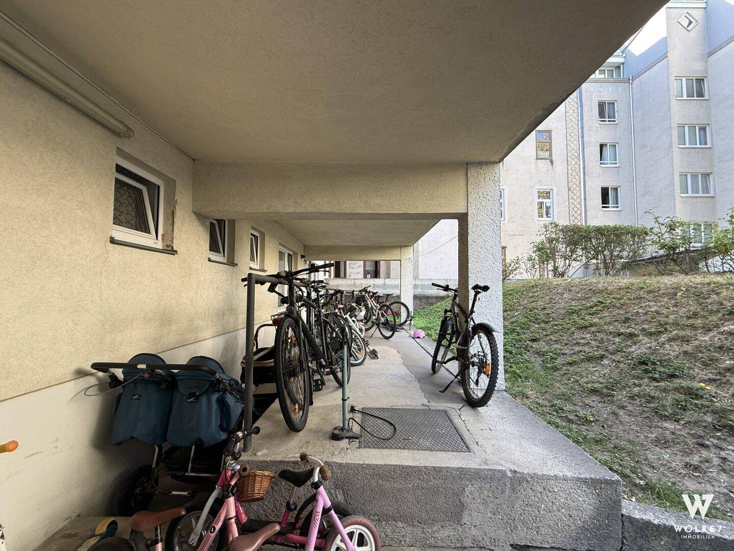 Überdachter Außenbereich mit Fahrradabstellplätzen neben einem Wohngebäude.