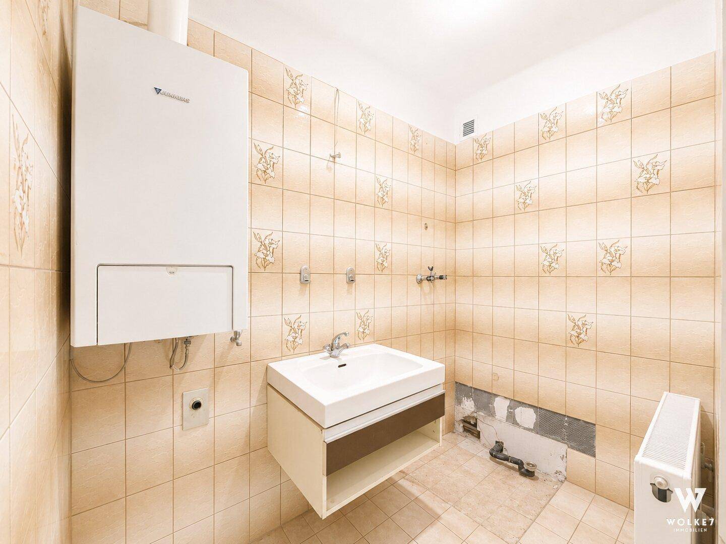 Badezimmer oder Hauswirtschaftsraum mit älteren Fliesen und Boiler, benötigt Modernisierung.