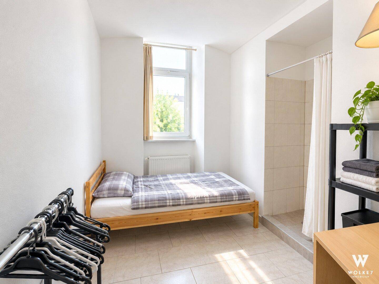 Helles Schlafzimmer mit Einzelbett, Fliesenboden und integrierter Duschkabine.