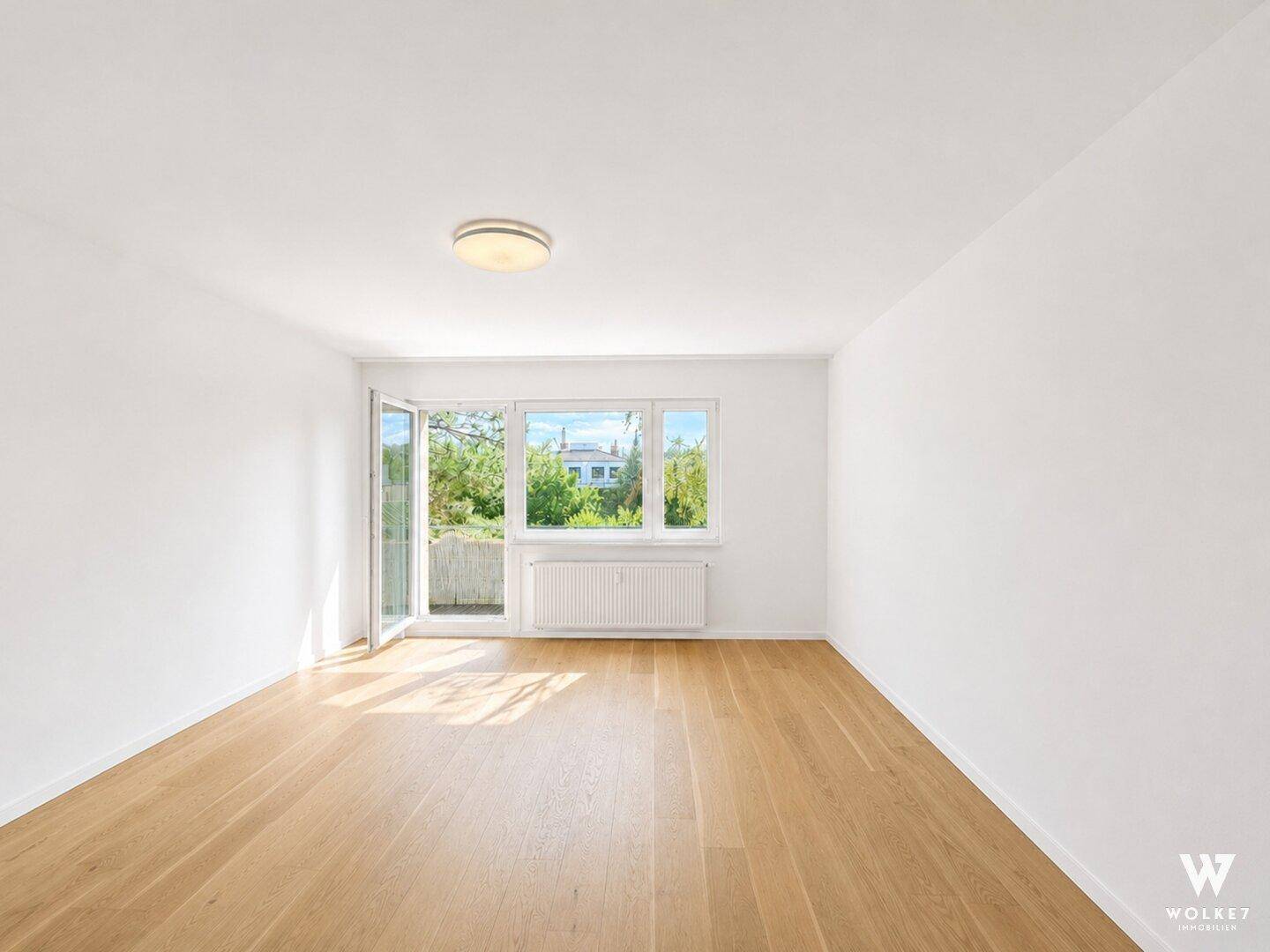 Helles, leeres Zimmer mit Holzboden und Zugang zu einem Balkon.