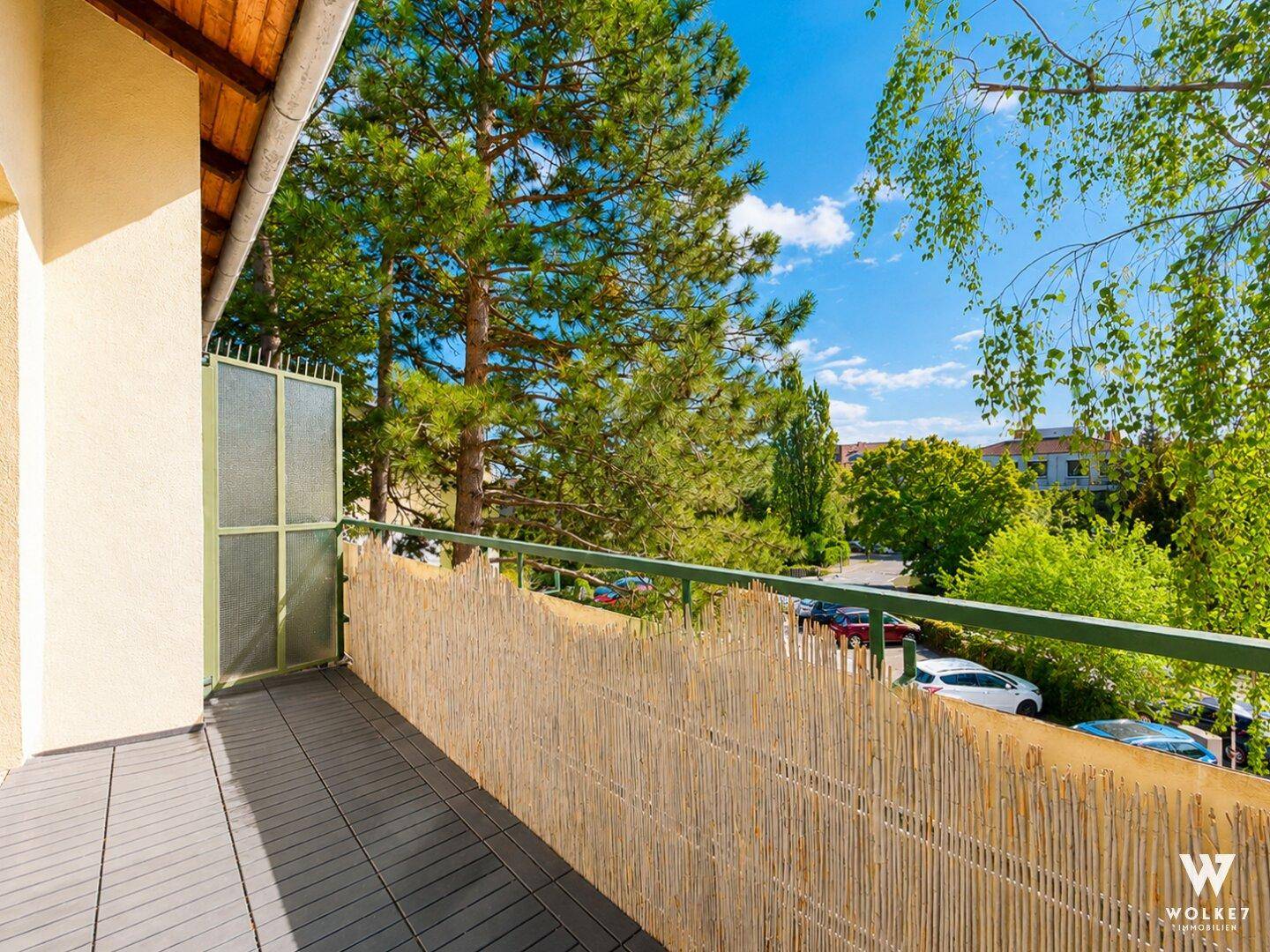 Heller Balkon mit modernem Bodenbelag und natürlichem Sichtschutz aus Bambus.