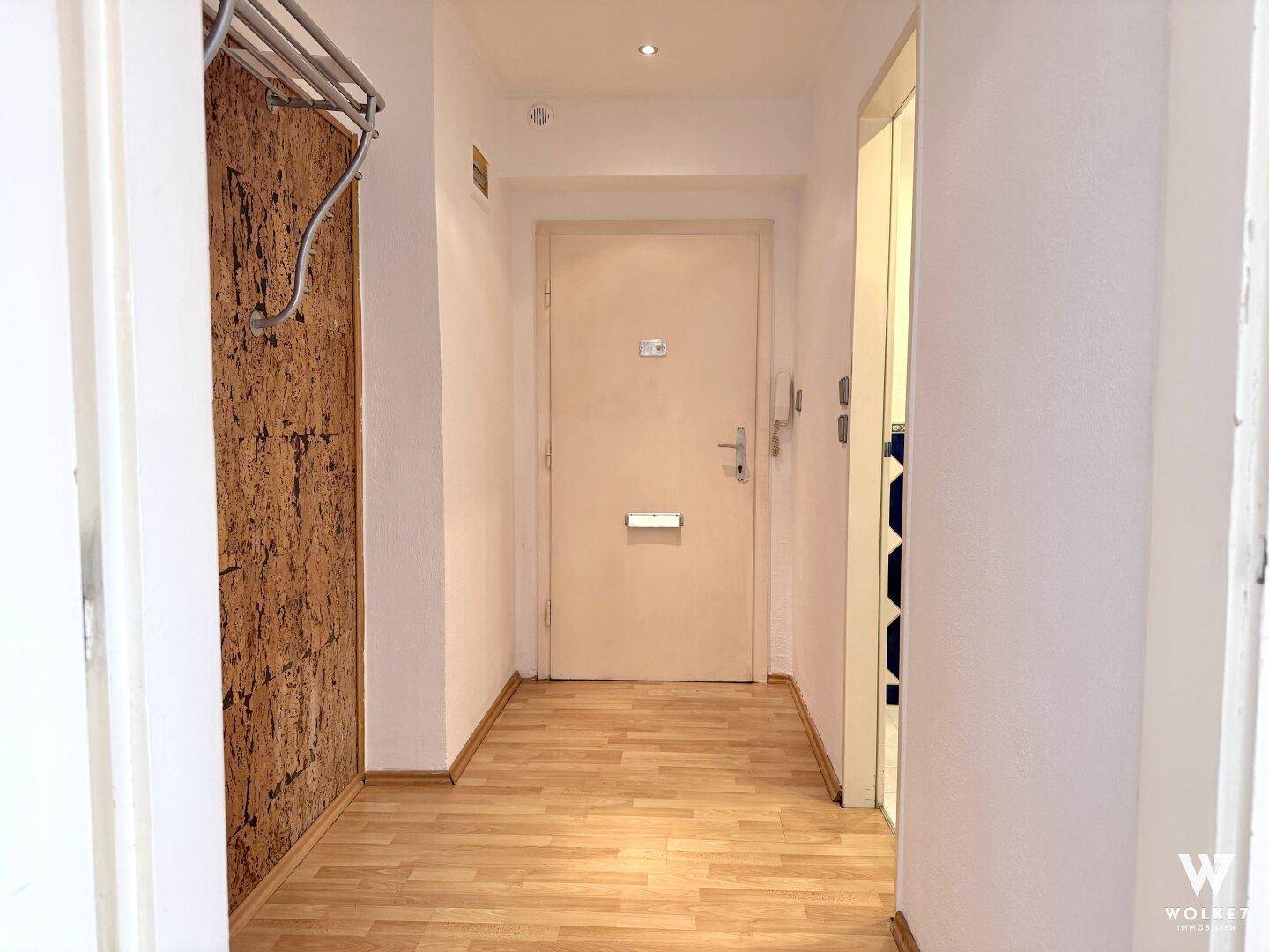 Lichtdurchfluteter Eingangsbereich mit Laminatboden, Korkwand und der Wohnungseingangstür.