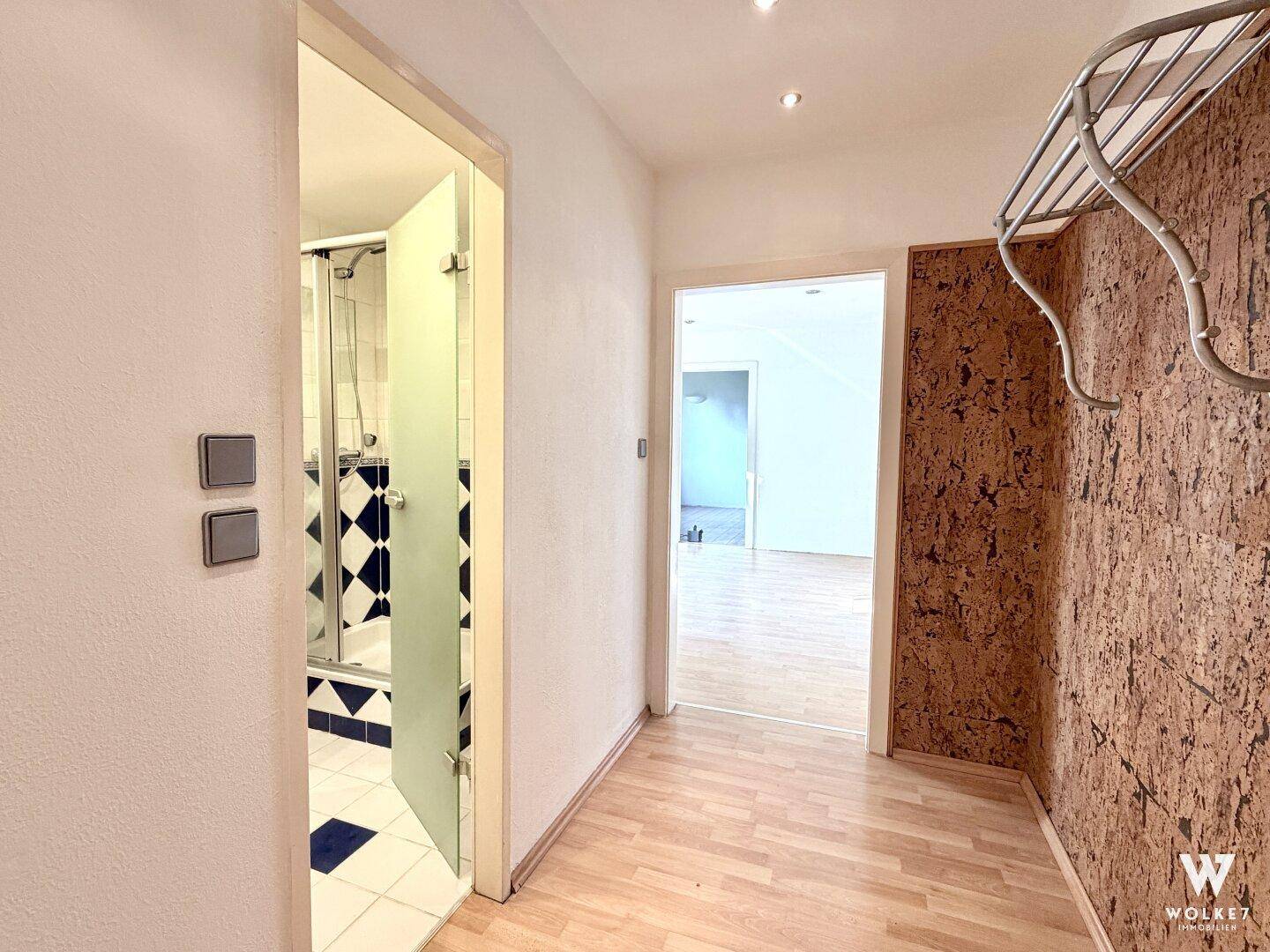 Heller Flur mit Laminatboden, dekorativer Korkwand und Zugang zu einem Badezimmer mit Dusche.