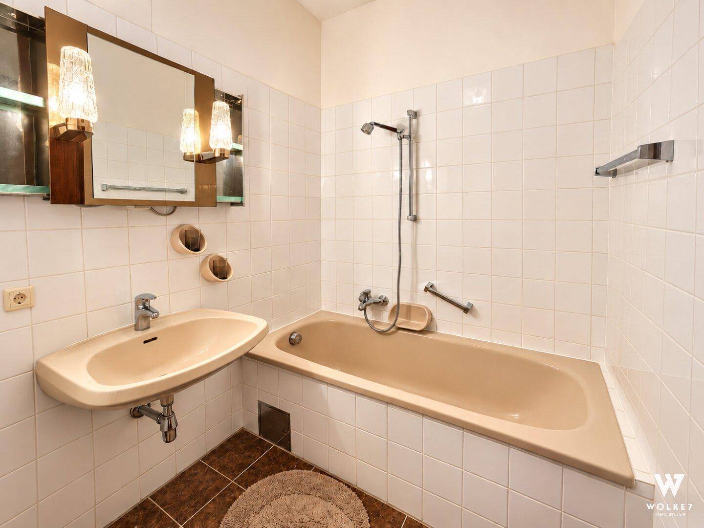 Badezimmer im Stil der 80er Jahre mit beiger Badewanne, passendem Waschbecken und weißen Fliesen.