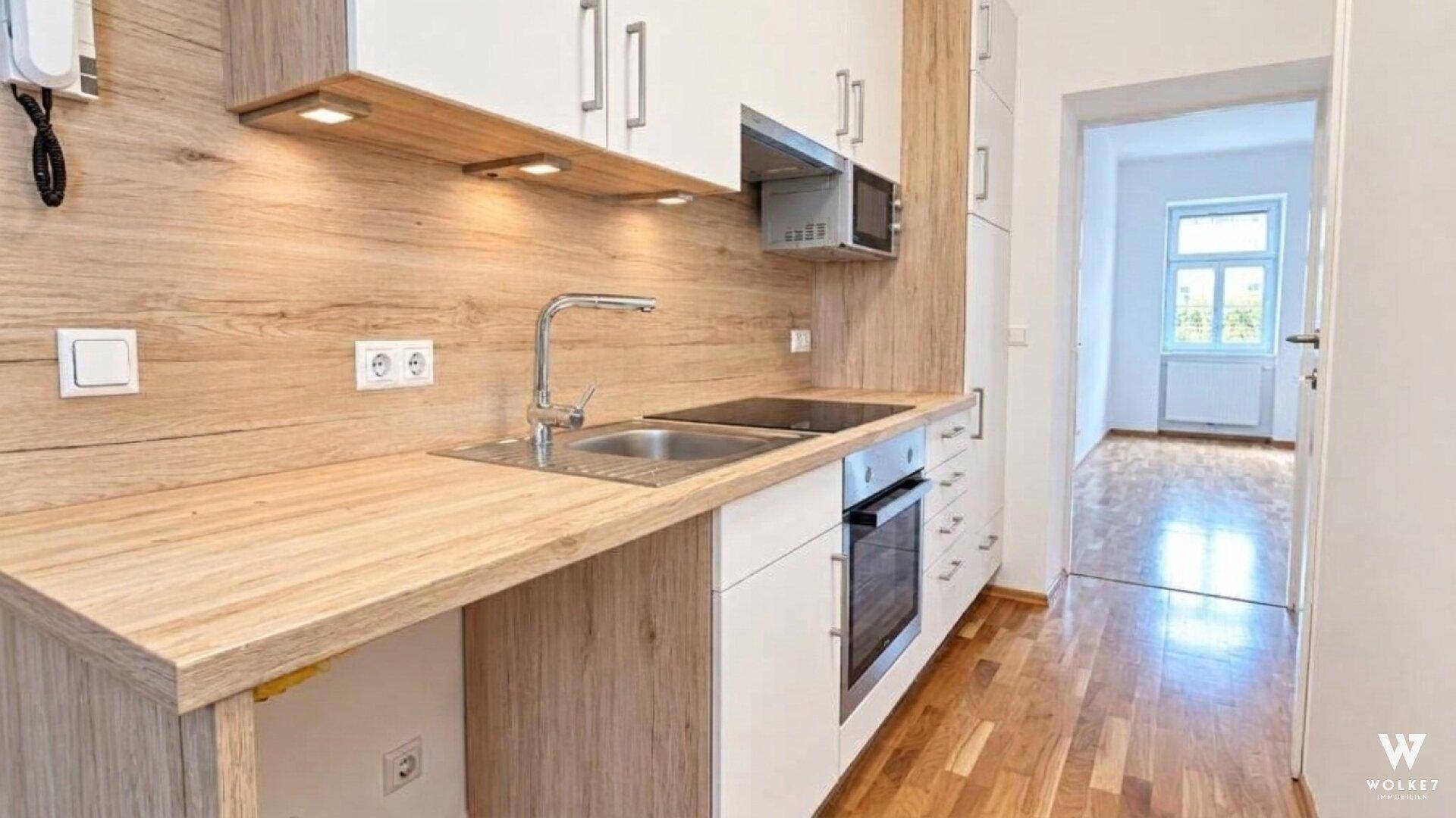 Moderne Einbauküche mit hellen Holzfronten, integrierten Geräten und Zugang zu einem weiteren Raum.