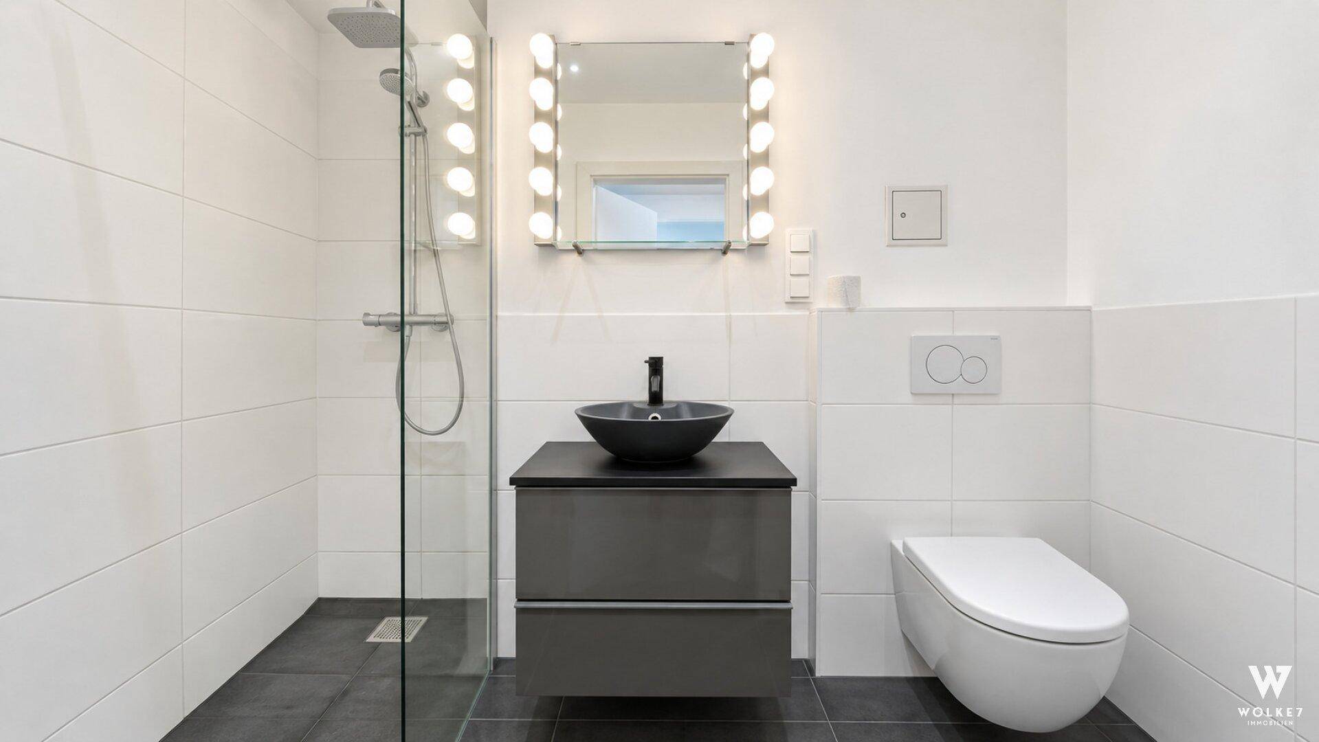 Modernes Badezimmer mit begehbarer Dusche, dunklen Fliesen und Wand-WC.