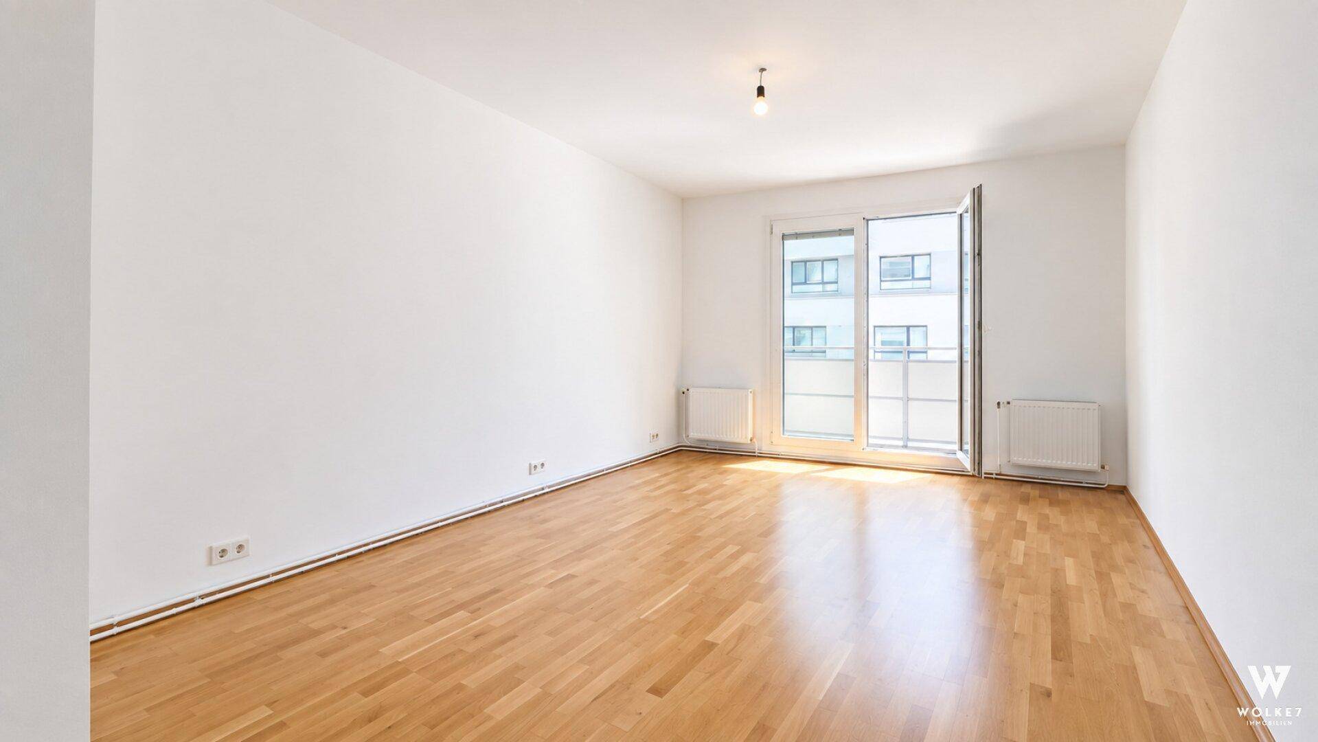Heller Raum mit Parkettboden und Zugang zu einem Balkon oder einer Terrasse.