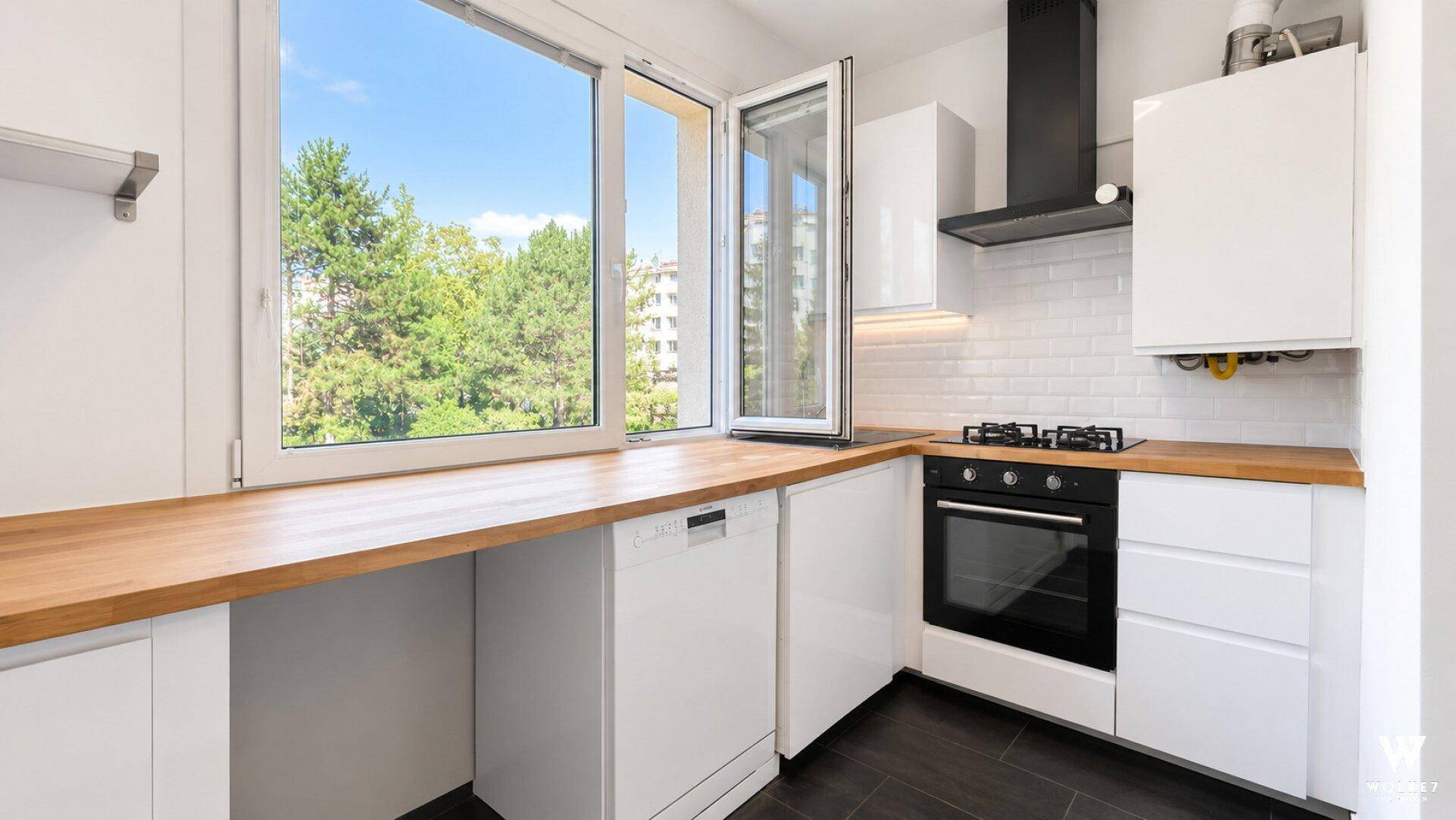 Moderne Küche mit weißen Schränken, Holzarbeitsplatte und großem Fenster mit Grünblick.