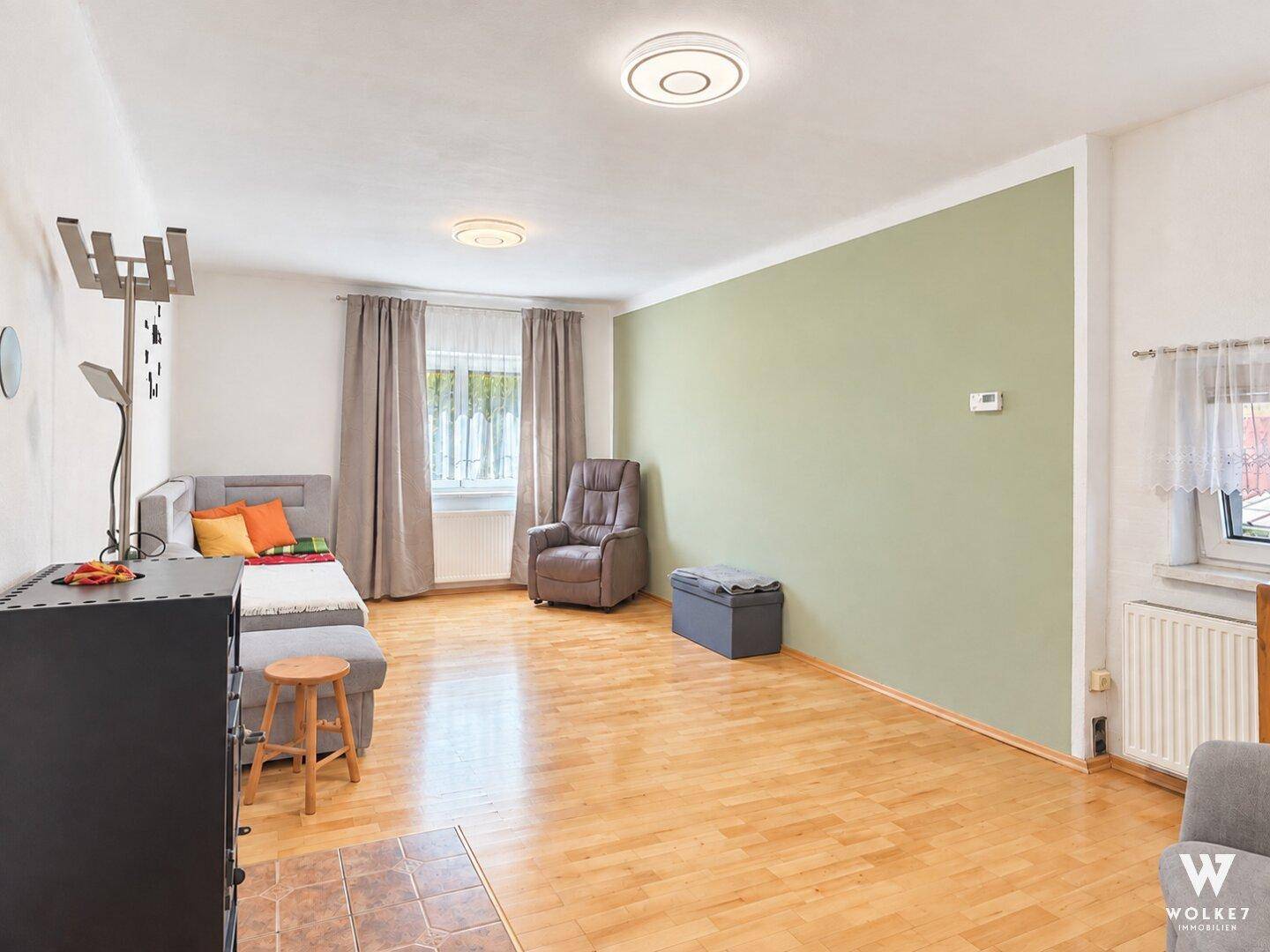 Helles Wohnzimmer mit Holzparkettboden, Kaminofen und einer Akzentwand in Pastellgrün.