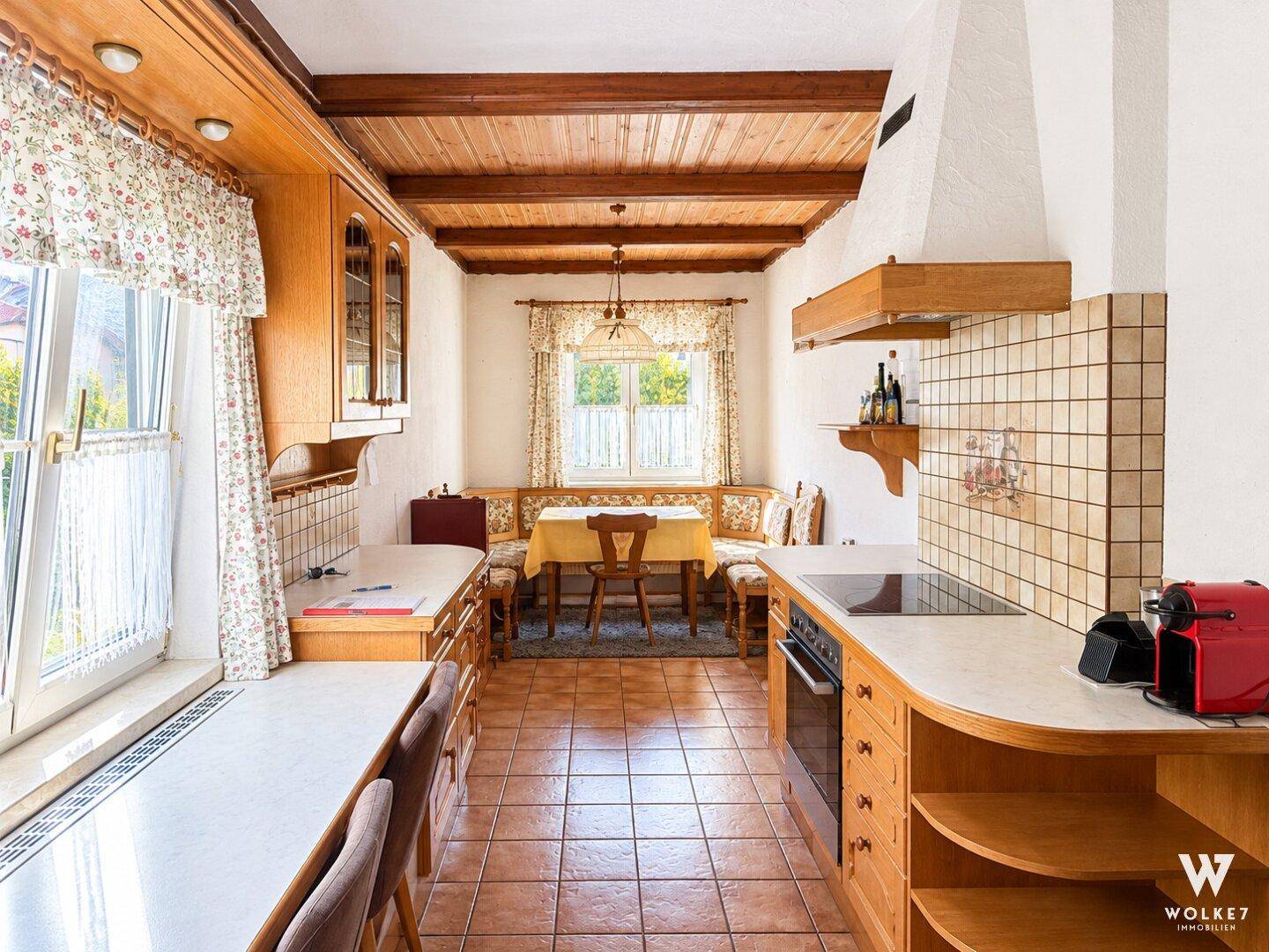 Traditionelle Küche mit Holzbalkendecke, Fliesenboden und gemütlicher Essecke am Fenster.