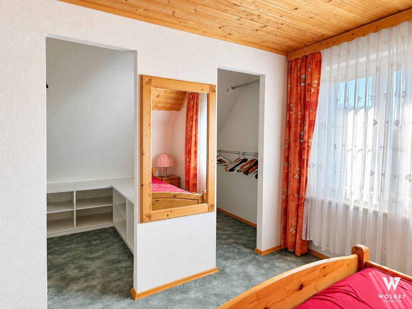 Schlafzimmer mit Teppichboden, Holzdecke und integriertem Ankleidebereich mit Spiegel.