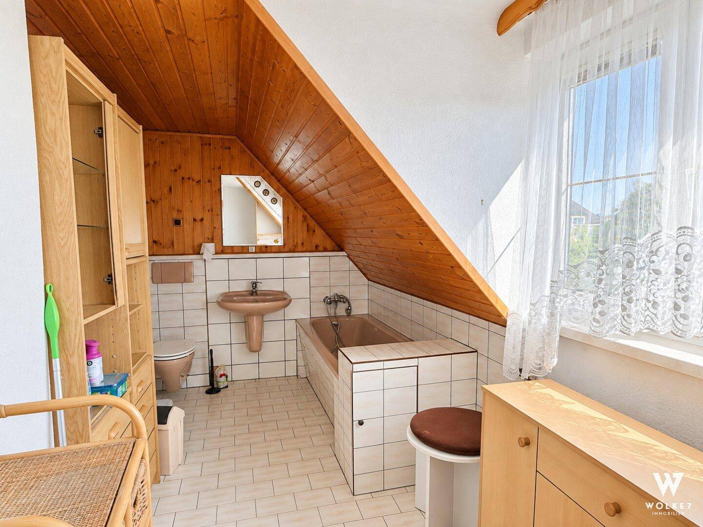 Badezimmer im Dachgeschoss mit Badewanne, Fliesenboden und Holzverkleidung an der Decke.