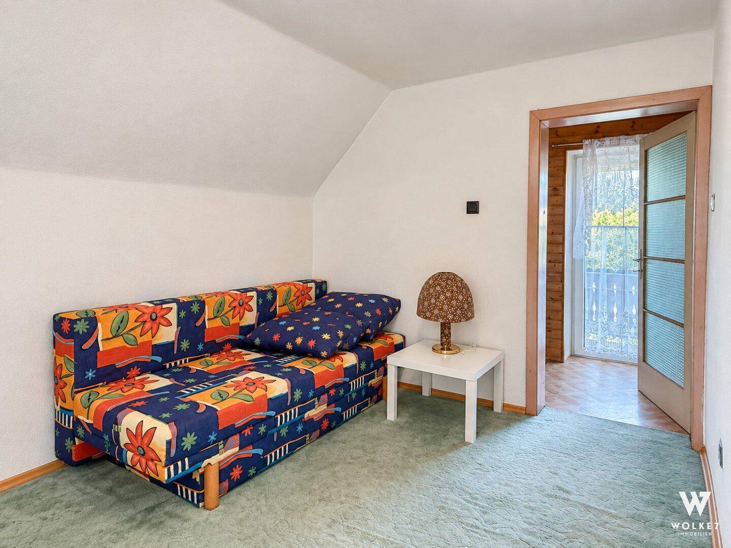 Helles Zimmer mit Schlafsofa, Teppichboden und Zugang zu einem Balkon.