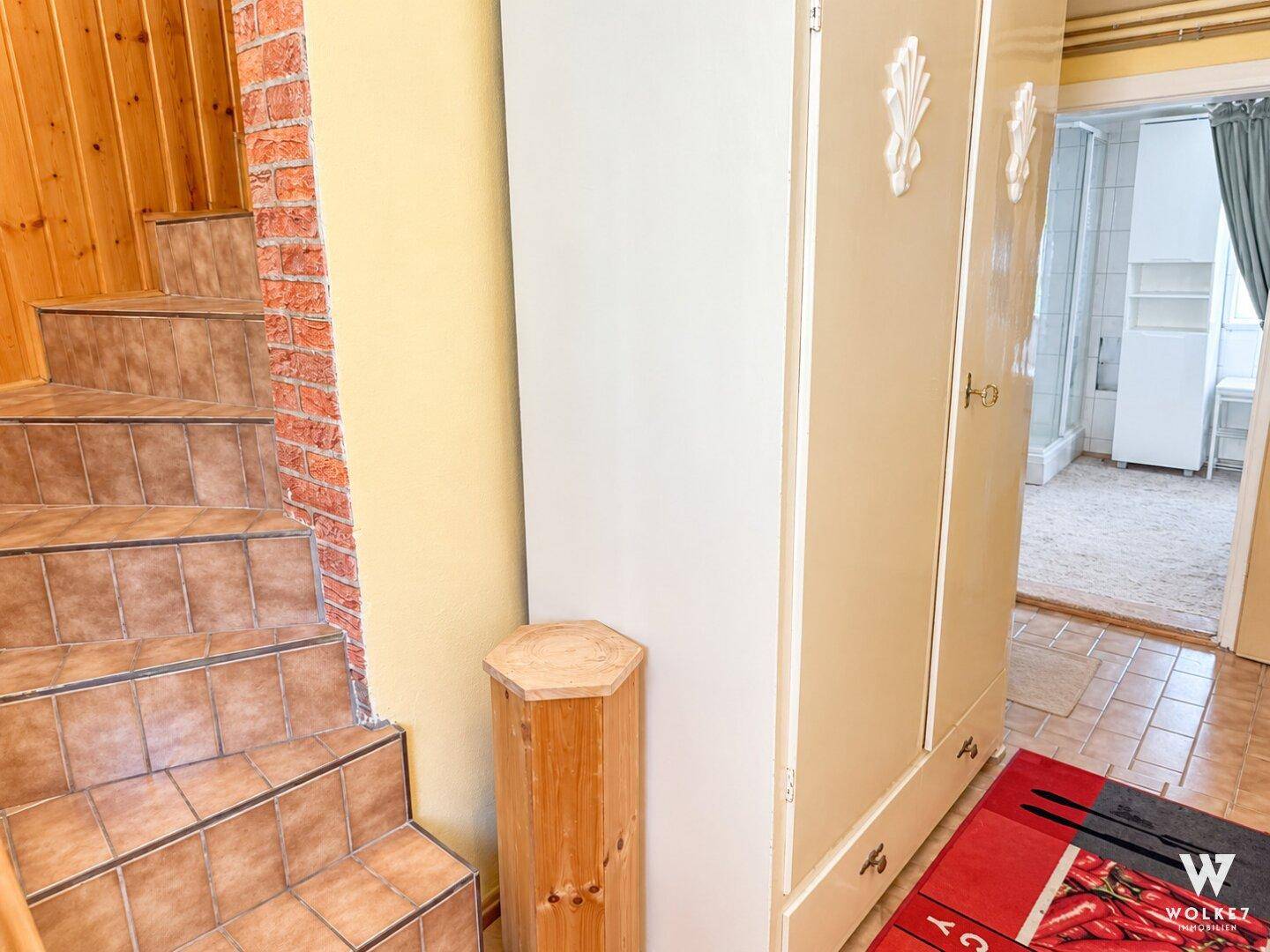 Flur mit gefliester Treppe, Schrank und Zugang zu weiteren Räumen.