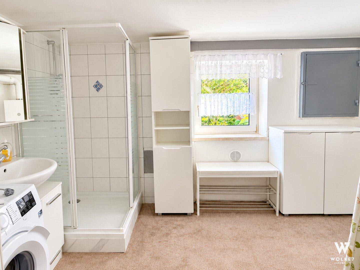 Modernisiertes Badezimmer im Keller mit Dusche, Waschmaschine und Fenster.