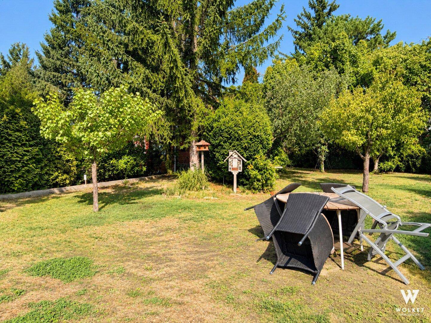 Gepflegter Gartenbereich mit Rasenfläche, Bäumen und Sitzgelegenheiten im Freien.