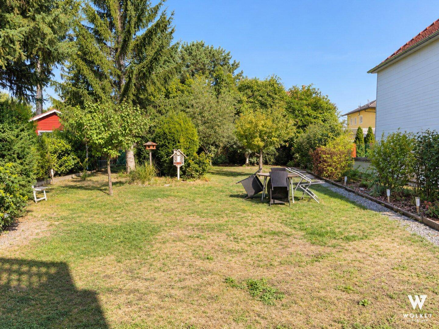 Weitläufiger Garten mit Rasenfläche, umgeben von Bäumen und Sträuchern, ideal zum Entspannen.