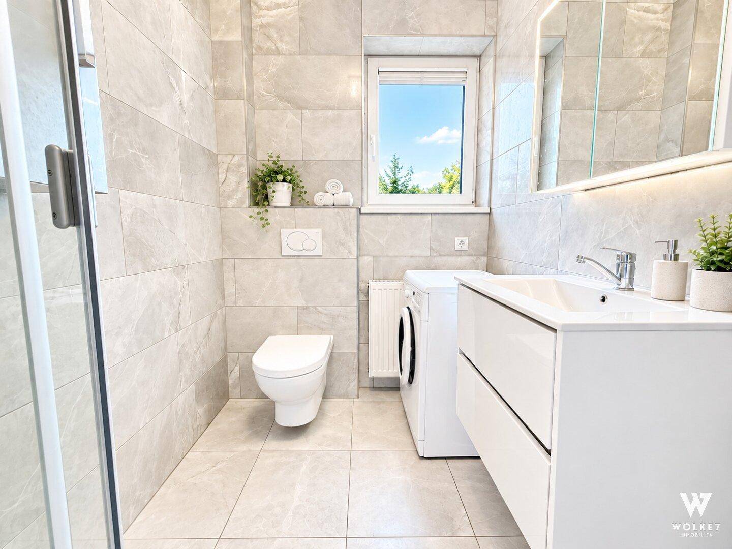 Modernes Badezimmer mit großformatigen grauen Fliesen, wandhängendem WC und Fenster.