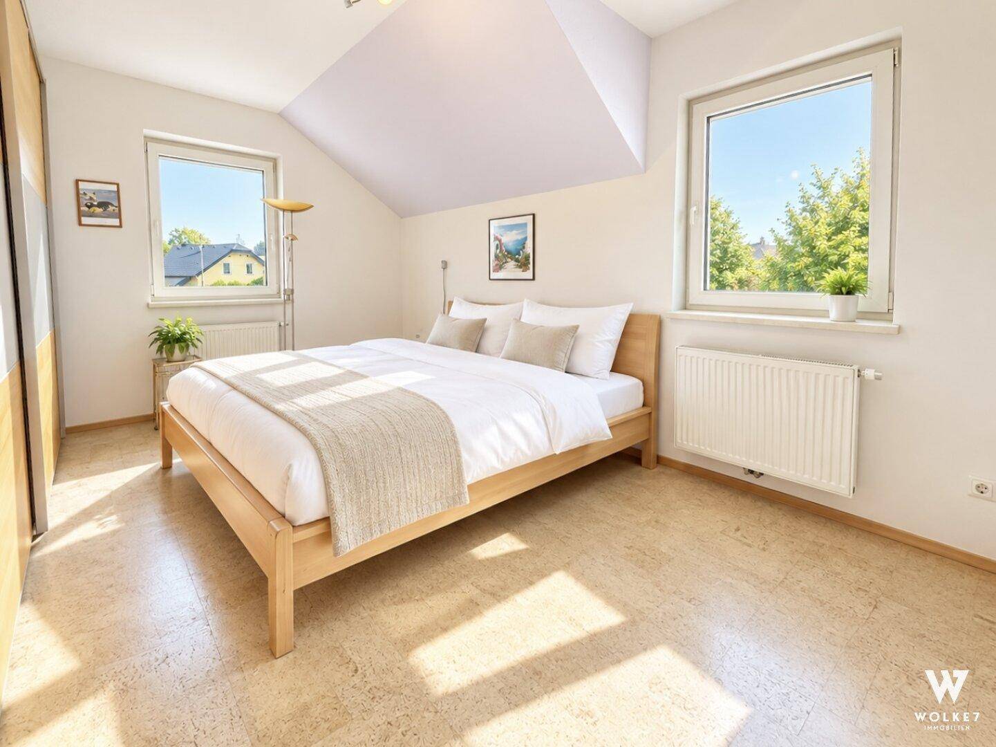 Helles Schlafzimmer mit Holzbett, großen Fenstern und schräger Decke im Dachgeschoss.