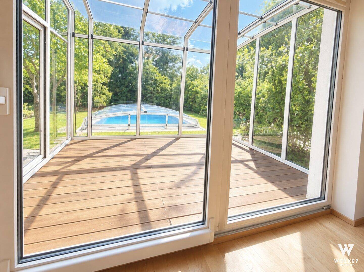 Heller Wintergarten mit Holzboden und Panoramablick auf den Garten und den Swimmingpool.