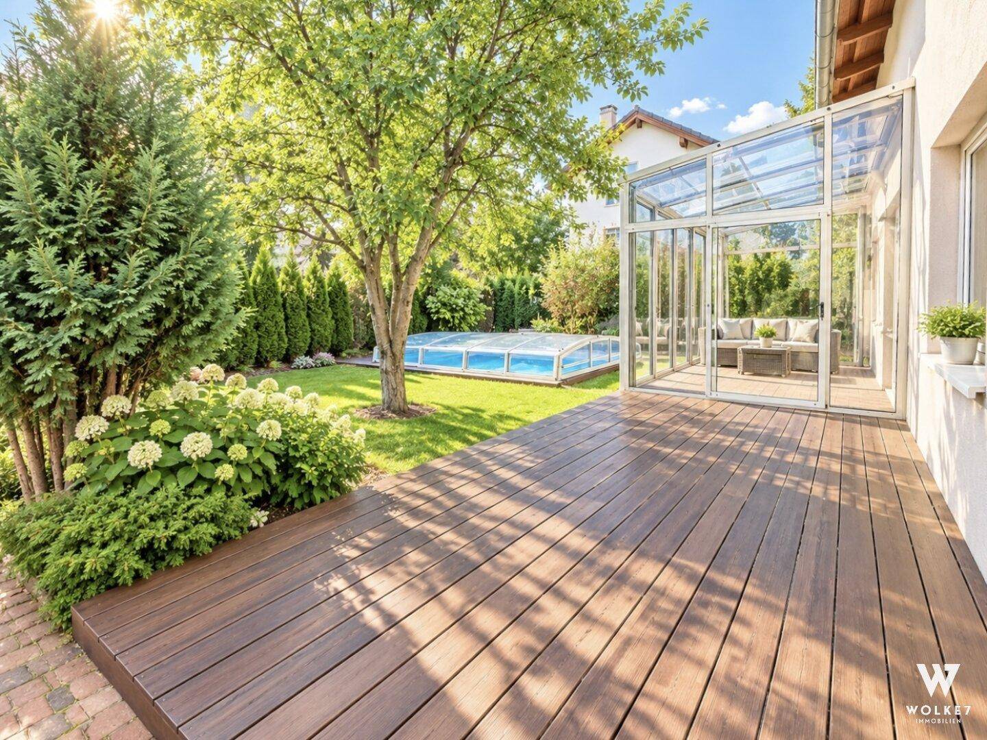 Sonnige Holzterrasse mit Blick auf den Garten, Wintergarten und den überdachten Swimmingpool.