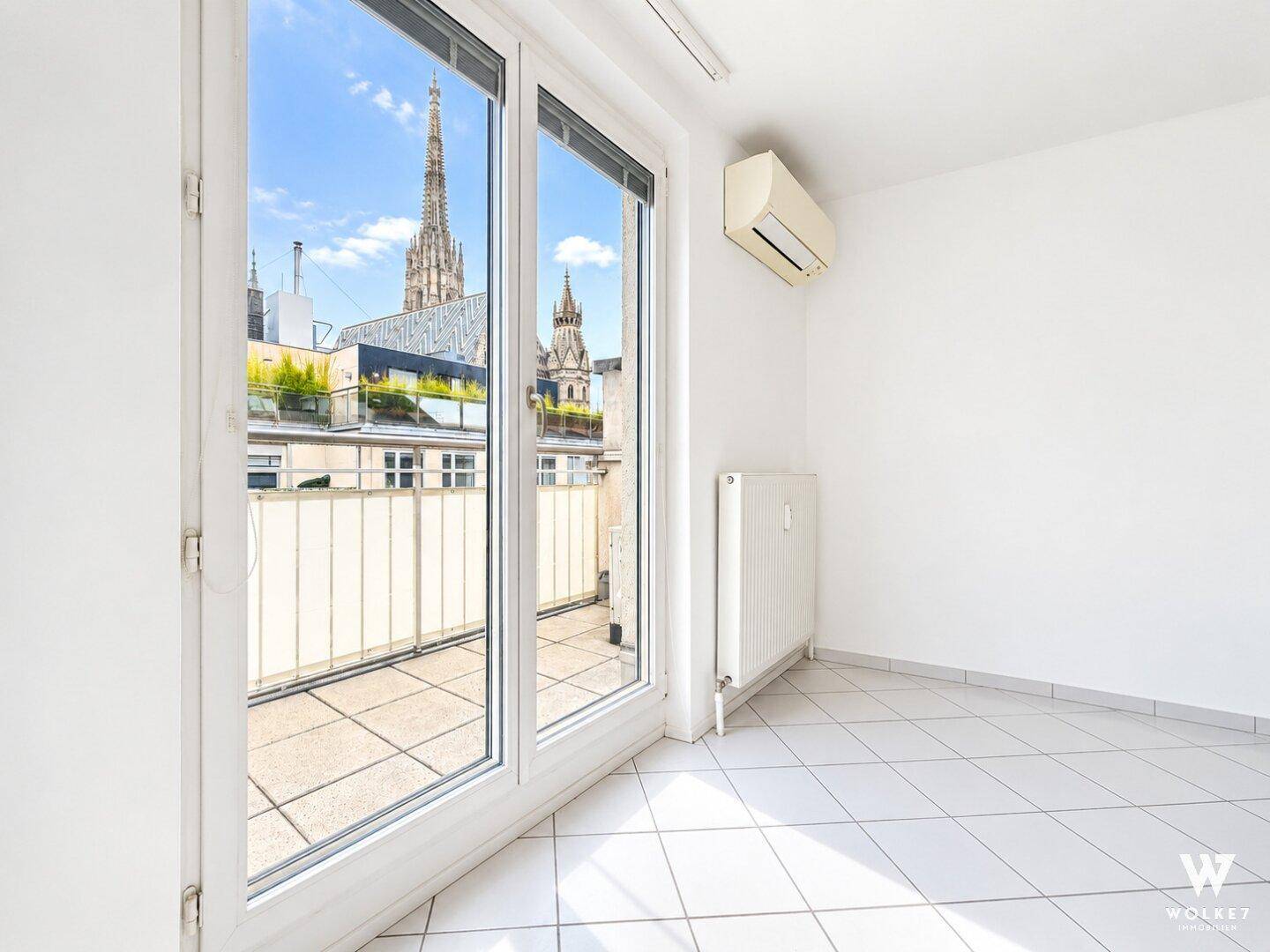 Heller Raum mit Fliesenboden, Klimaanlage und großem Fenster mit Blick auf den Stephansdom.