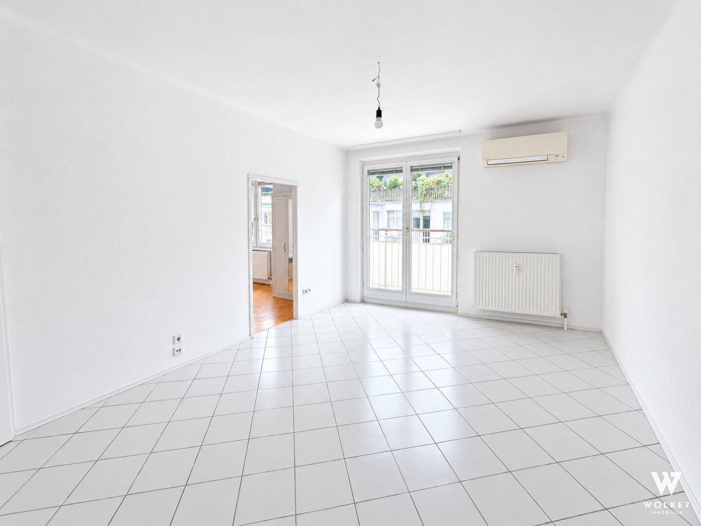 Heller Wohnraum mit weißen Fliesen, Klimaanlage und Zugang zu einem französischen Balkon.
