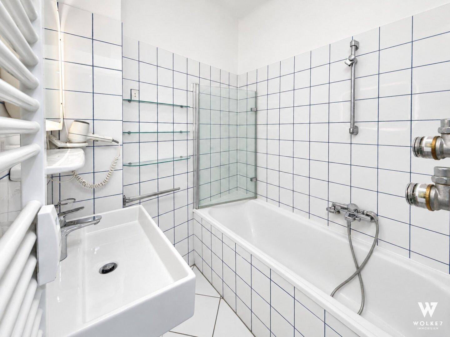 Badezimmer mit weißen Fliesen, Badewanne mit Duschwand und einem Waschbecken.