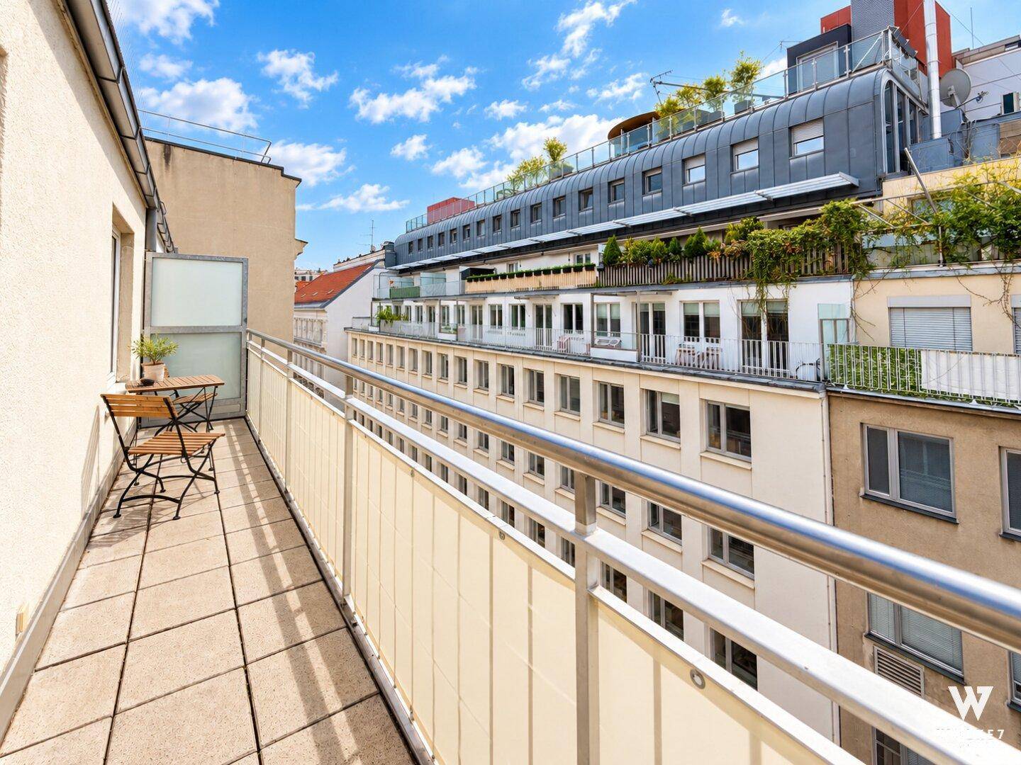 Langer Balkon mit Fliesenboden und Blick auf die umliegenden Gebäude und Dächer.