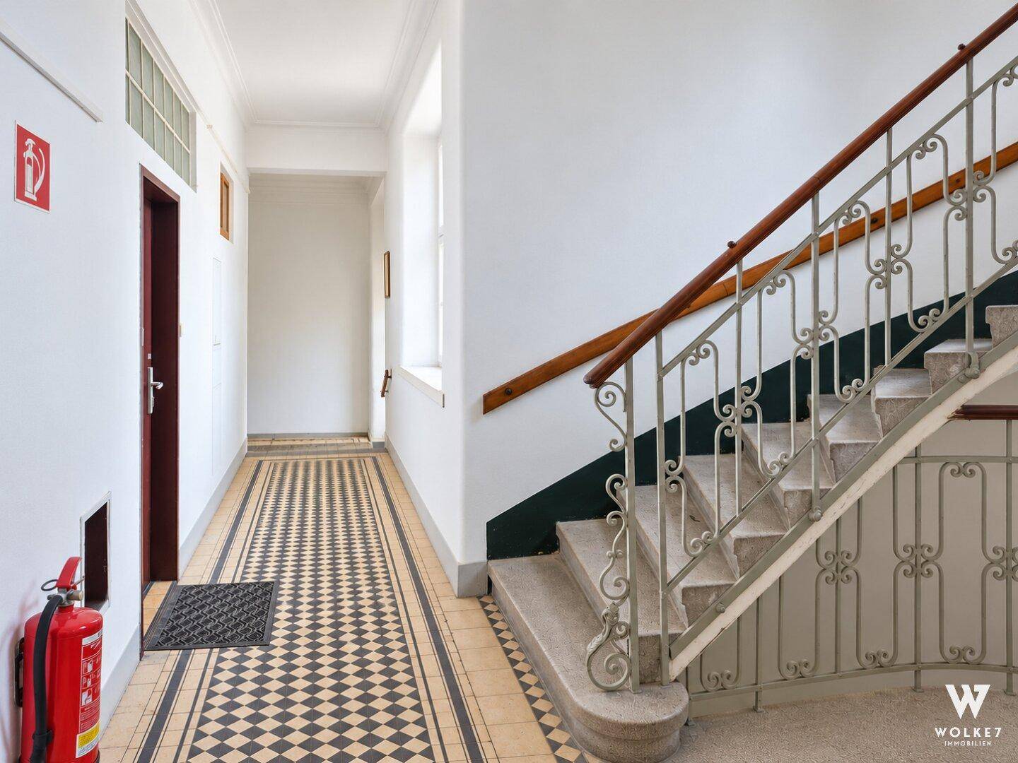 Treppenhaus mit kunstvollem Geländer und einem Flur mit auffälligem Schachbrettmuster-Fliesenboden.