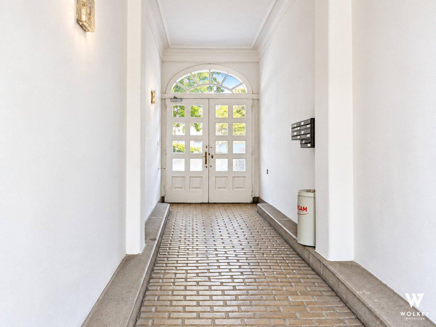 Heller Eingangsbereich mit gemustertem Fliesenboden und großen Doppeltüren zum Außenbereich.