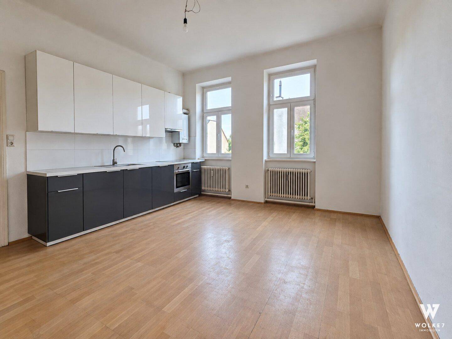 Moderne Küche mit weißen Oberschränken, grauen Unterschränken und hellem Parkettboden.