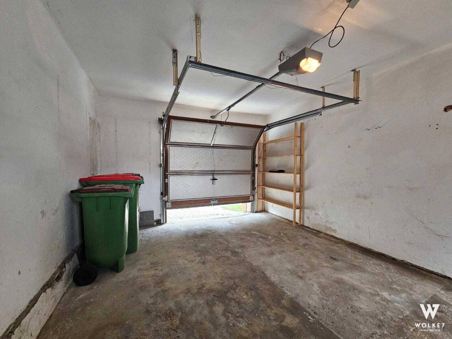 Geräumige Garage mit geöffnetem Tor, Betonboden und Regalen an der Wand.