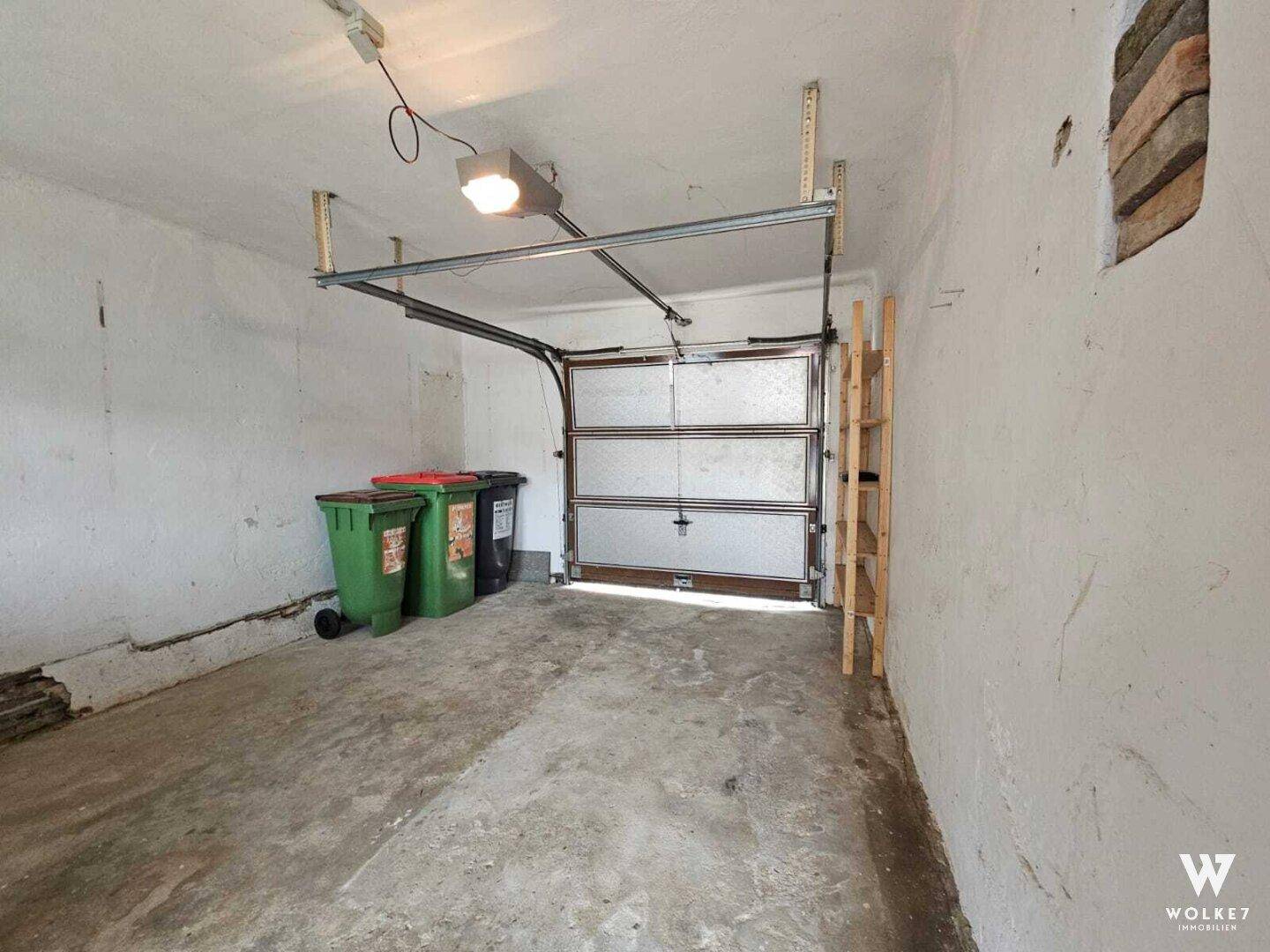 Innenansicht einer Garage mit Betonboden, weiß gestrichenen Wänden und Garagentor.