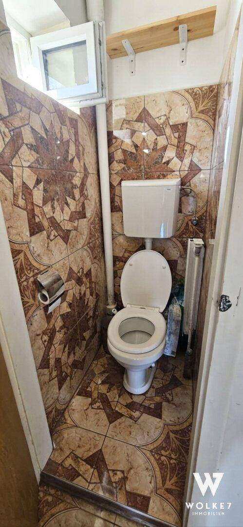 Kleiner Toilettenraum mit gemusterten Fliesen, WC und einem kleinen Fenster.