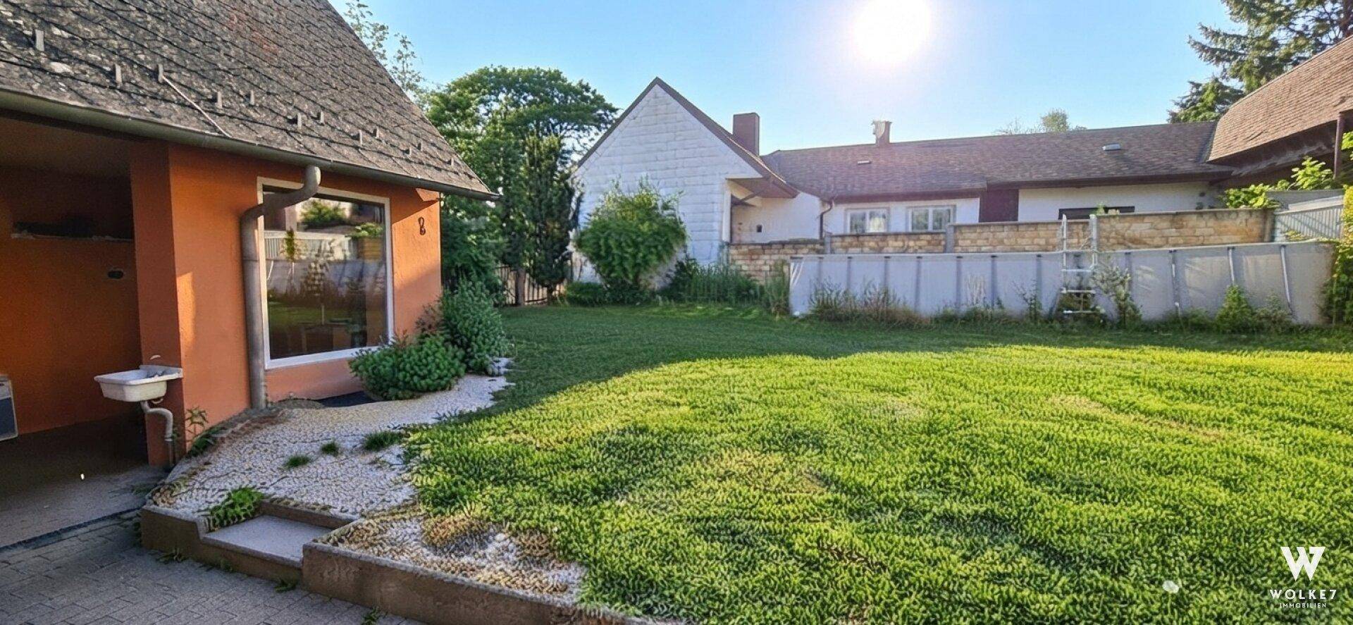 Großer Gartenbereich mit Rasenfläche, Aufstellpool und Nebengebäude an einem sonnigen Tag.