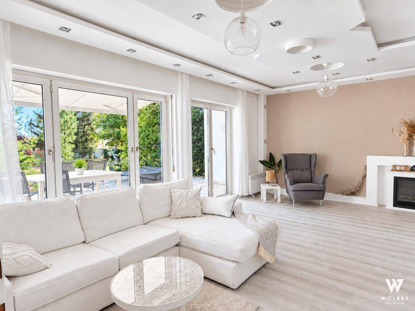 Helles Wohnzimmer mit weißem Sofa, modernem Kamin und direktem Zugang zur Terrasse und zum Garten.