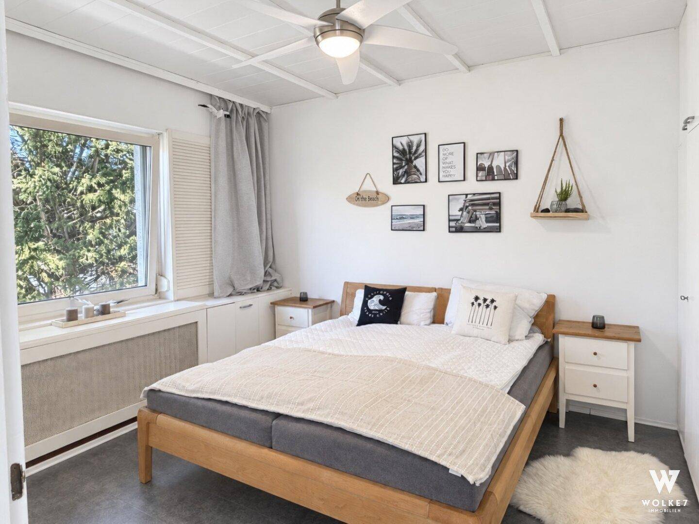 Gemütliches Schlafzimmer mit Doppelbett, Deckenventilator und Blick auf grüne Bäume.