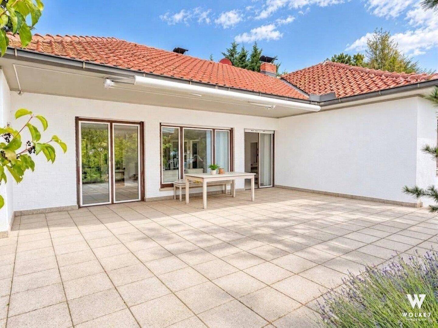 Große geflieste Terrasse mit Esstisch und Stühlen, umgeben von einem gepflegten Gartenbereich.