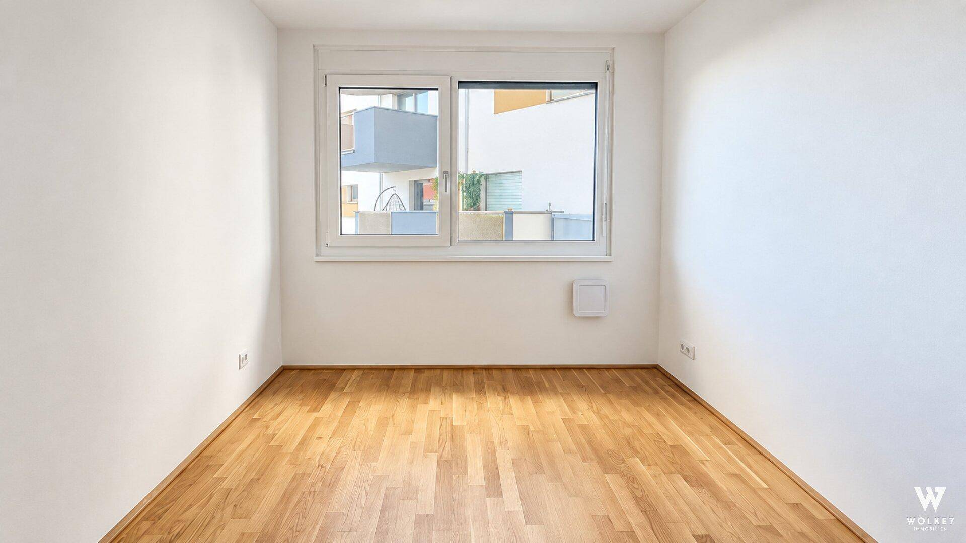 Heller, leerer Raum mit Holzboden und großem Fenster, ideal als Schlaf- oder Arbeitszimmer.
