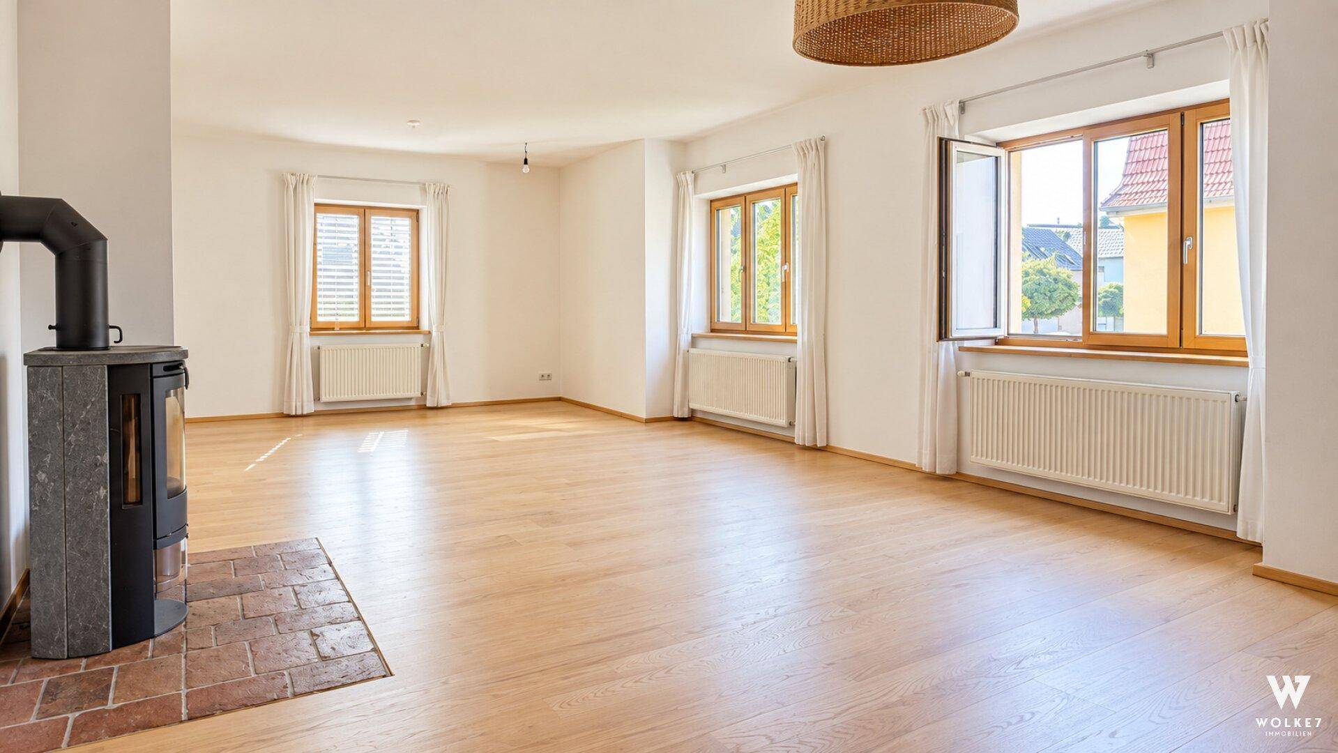 Geräumiger, unmöblierter Wohn-Essbereich mit hellem Holzfußboden und traditionellem Kaminofen.
