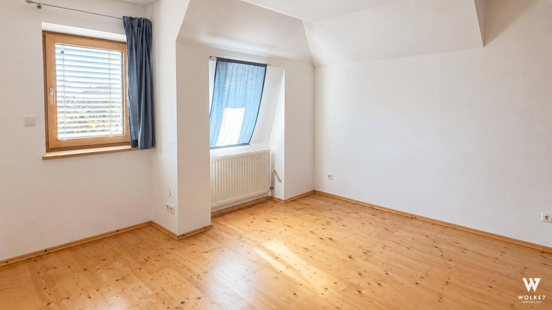 Helles Schlafzimmer im Dachgeschoss mit Holzplankenboden und zwei Fenstern für viel Tageslicht.