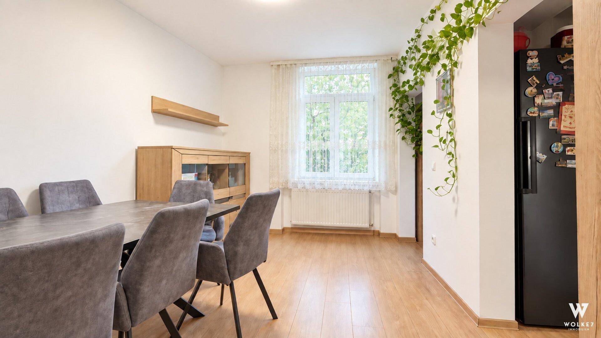 Essbereich mit Holzboden, Esstisch und Stühlen, angrenzend an einen Kühlschrank, ideal für Familienmahlzeiten.