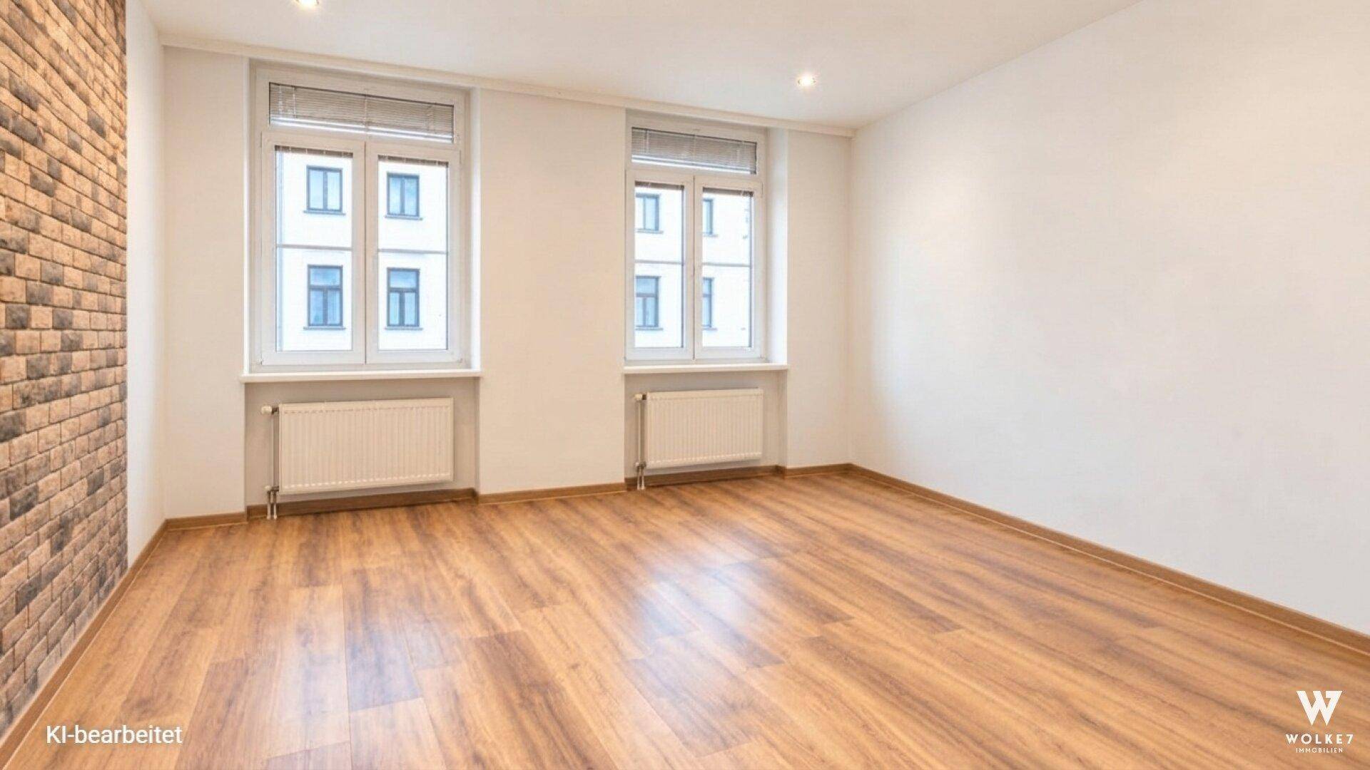 Leeres Zimmer mit Holzboden, weißen Wänden und zwei großen Fenstern, bereit zur individuellen Gestaltung.
