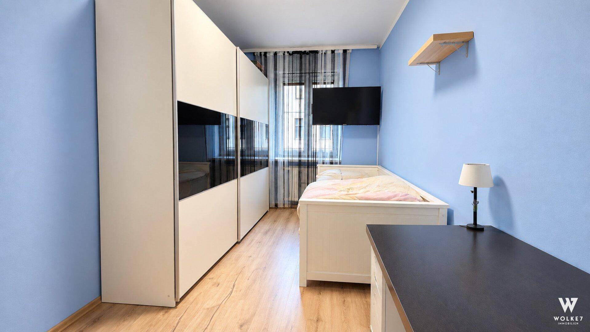 Schlafzimmer mit blau gestrichenen Wänden, Einzelbett und großem Kleiderschrank, bietet viel Stauraum.